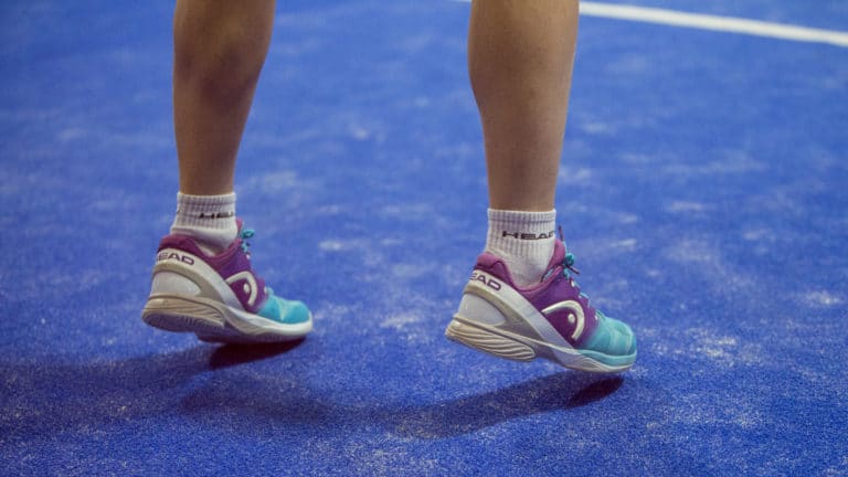 Zwei Füße kurz vorm Absprung auf blauem Padel Court
